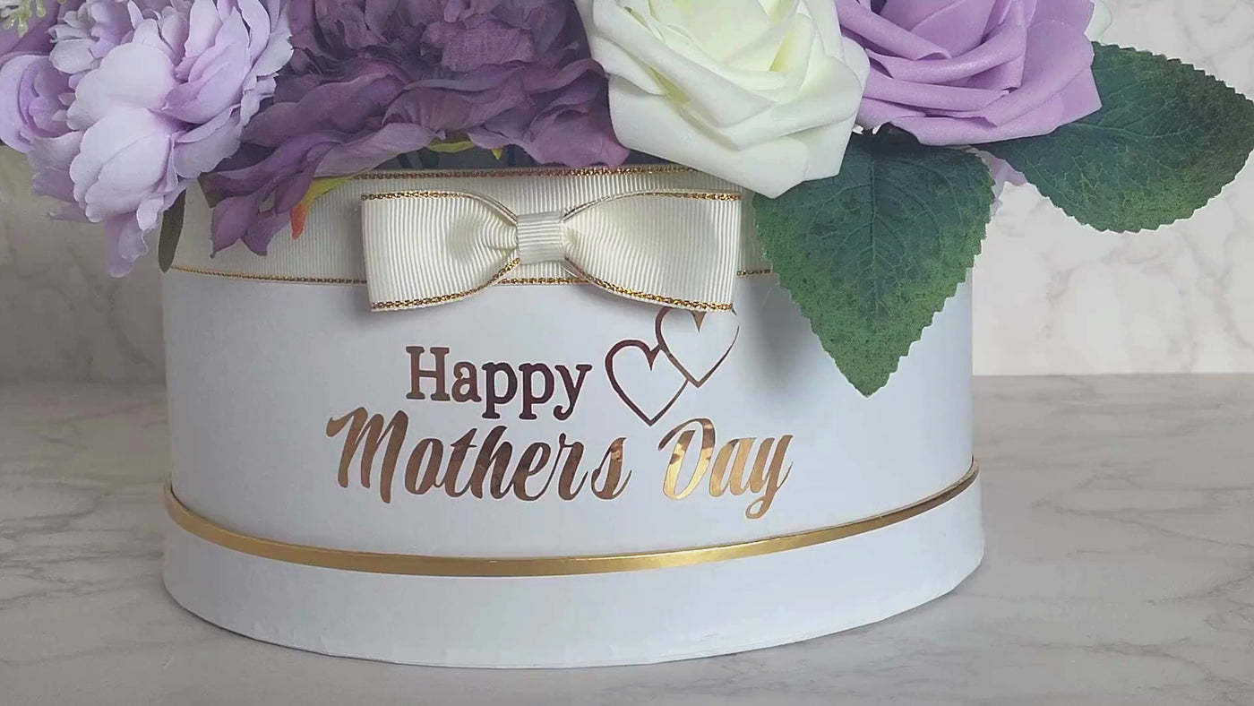 This stunning foam rose arrangement, made with lifelike fabric and soft foam purple and white roses, is a true embodiment of elegance. The beautiful assortment of pink and white flowers, carefully arranged in a white hat box with gold trimming, is sure to brighten up anyone's day. With the heartfelt "Happy Mother's Day" message and the lovely bow, it makes for a perfect gift