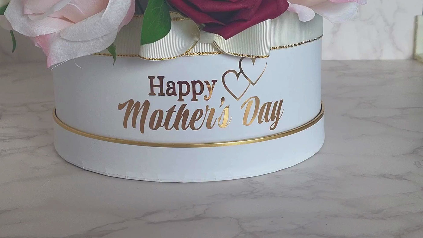 This stunning foam rose arrangement, made with lifelike fabric and soft foam red and white roses, is a true embodiment of elegance. The beautiful assortment of pink and white flowers, carefully arranged in a white hat box with gold trimming, is sure to brighten up anyone's day. With the heartfelt "Happy Mother's Day" message and the lovely bow, it makes for a perfect gift to show your love and appreciation to your mother. to show your love and appreciation to your mother.